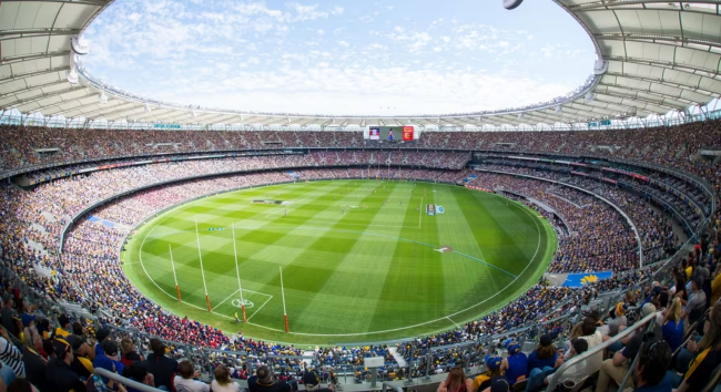澳洲 AFL 比賽現場，滿座的 Optus Stadium 觀眾席與橢圓形草地球場，展現澳式足球的熱烈氛圍。