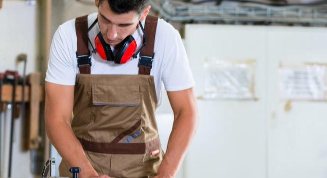 有一個身穿卡其色圍裙的男生在做櫥櫃工作 有黑色紅色耳機