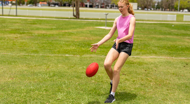 澳式足球 AFL 有一個身穿粉紅上背心的女生 黑色褲子在踢球