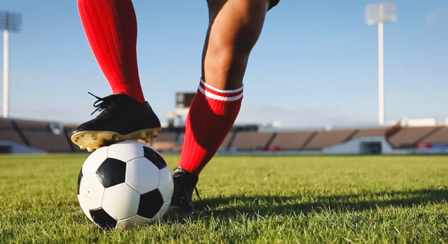 草地上有一個身穿紅色襪子加上黑色的鞋子在踢足球