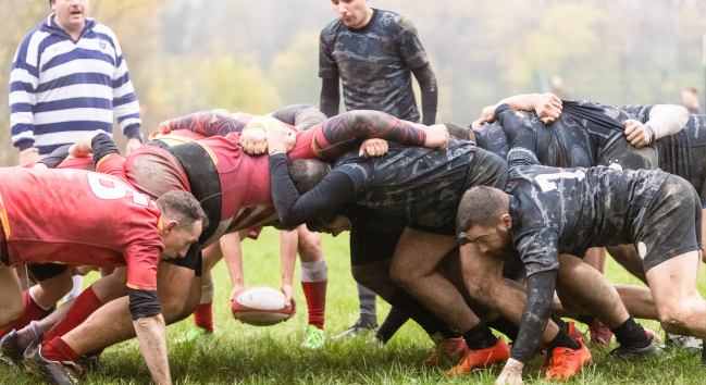 有兩個教練在盯著一群身穿紅色還有黑色衣服的人在玩rugby union
